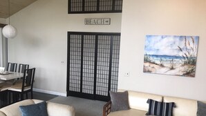 A living room with a beige sofa, a dining table with chairs, a painting of a beach scene, and a sign that reads "BEACH". - The San'Bar - Great Family Home Just A Short Walk To York's Beautiful Beaches (York)