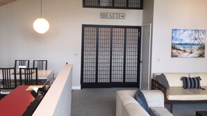 A room with a high ceiling, a ceiling fan, a sign reading "BEACH", a painting of a beach scene, a sofa with cushions, and a dining area with chairs and a table. - The San'Bar - Great Family Home Just A Short Walk To York's Beautiful Beaches (York)