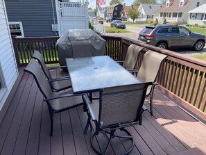 Eine Terrasse mit Tisch, Stühlen, einem Grill und Blick auf die Nachbarschaft.