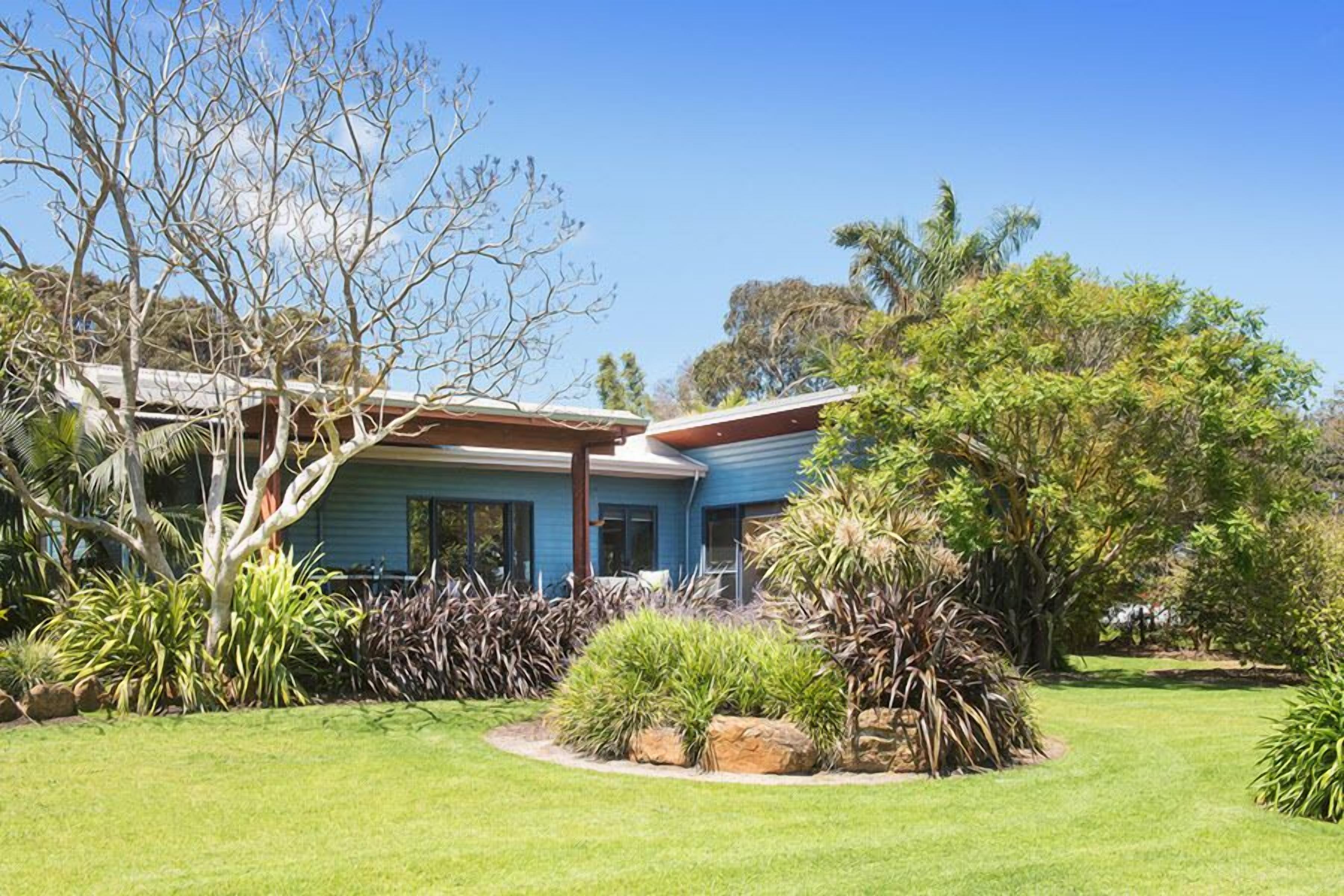 A house with a blue exterior, surrounded by a well-maintained garden with various plants and a lawn.