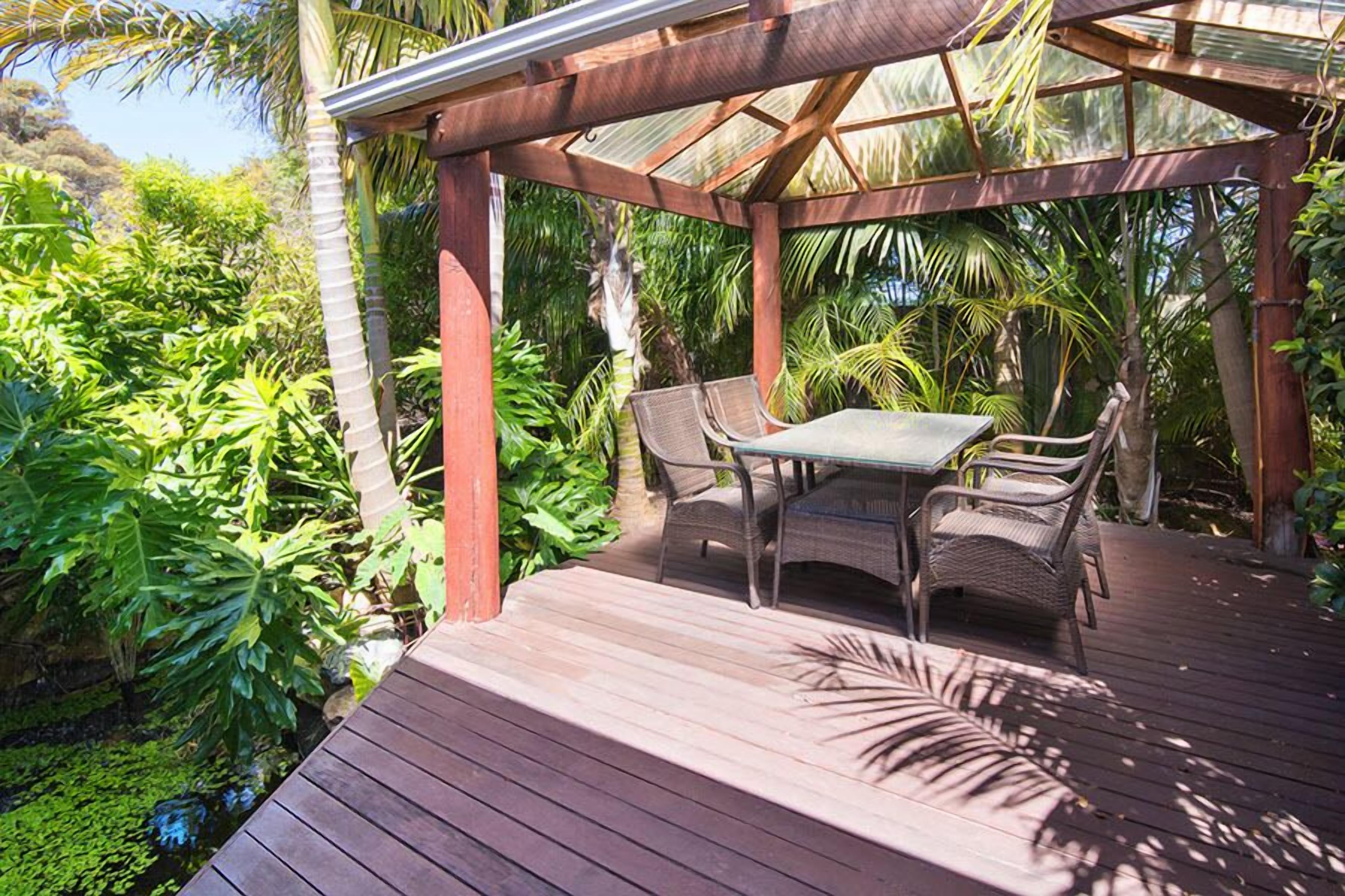 Una terraza de madera con una mesa y sillas, rodeada de abundante vegetación tropical.