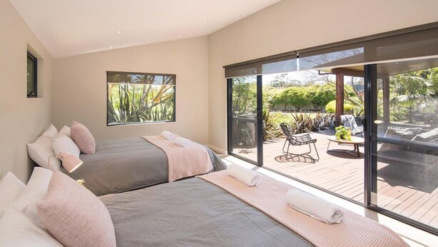 A modern bedroom with two beds, a large sliding glass door leading to an outdoor patio area.