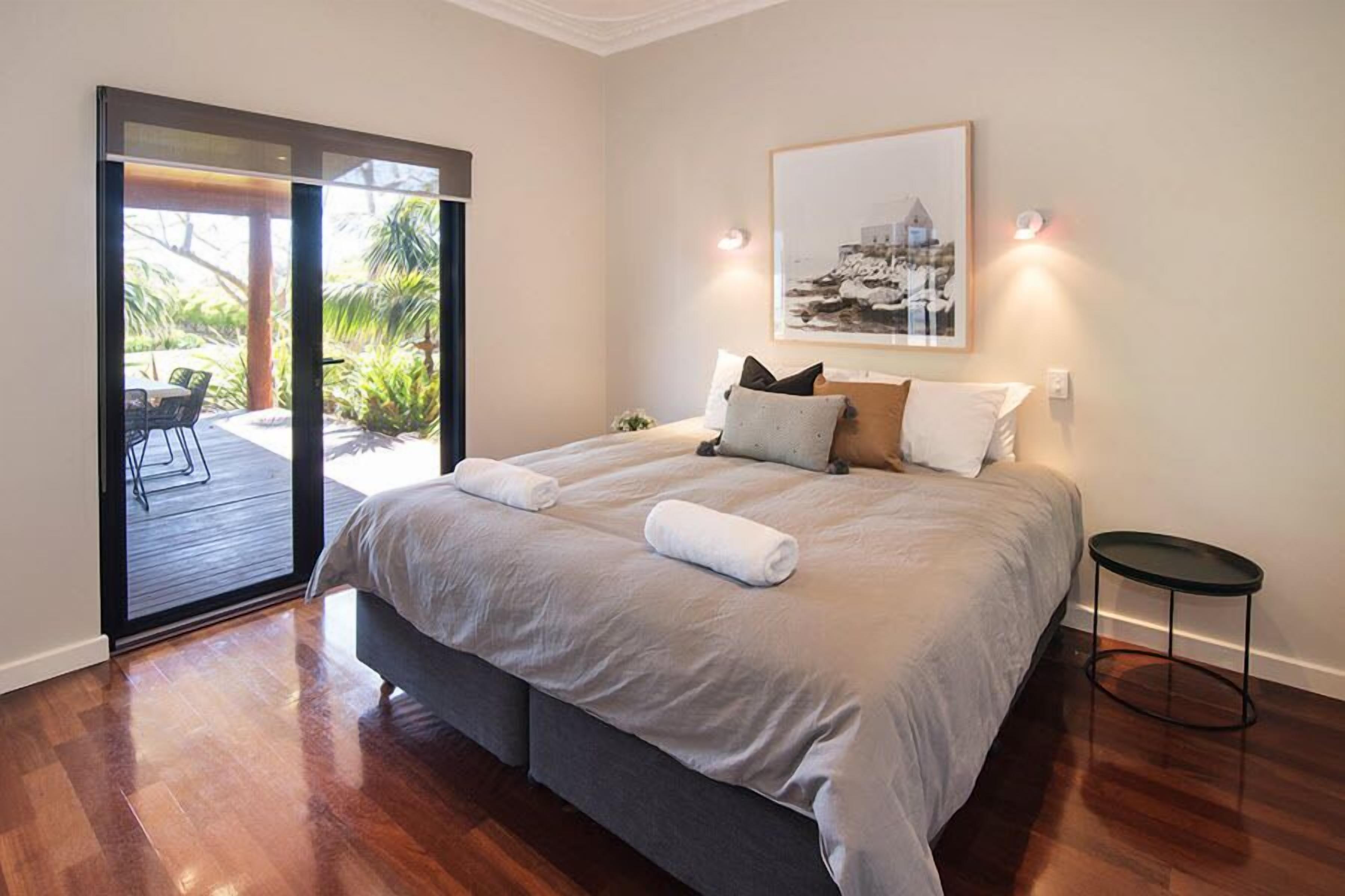 Een slaapkamer met een groot bed, een klein rond tafeltje en een schuifdeur die leidt naar een buitenruimte met terras en stoelen.