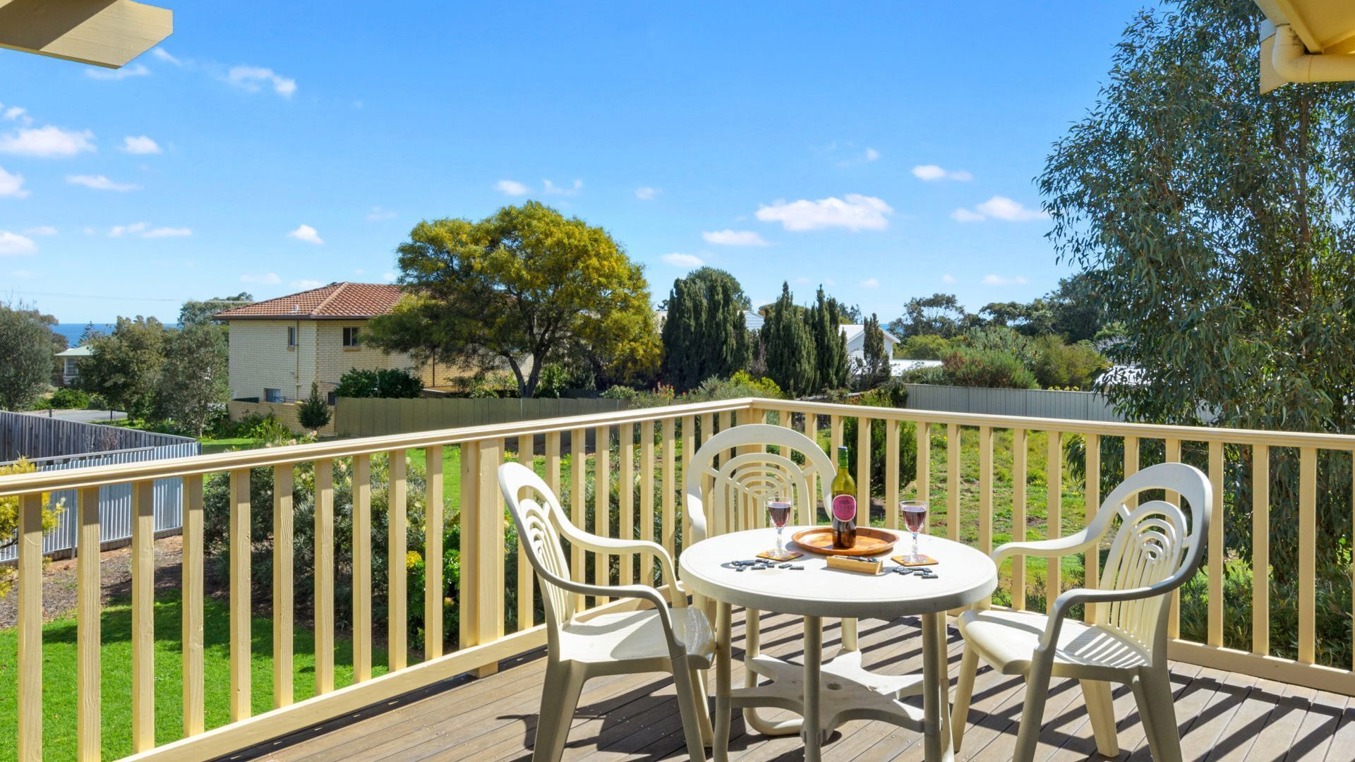 A deck with a round table and four chairs, surrounded by a wooden railing.