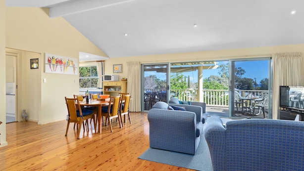 A spacious living area with a dining table, sofas, and a balcony with outdoor furniture. - 22 Broadbeach Drive Carrickalinga (CARRICKALINGA)