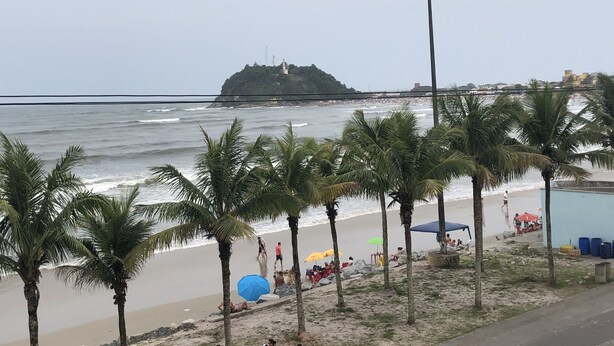 Una playa con palmeras, costa rocosa y una isla distante.