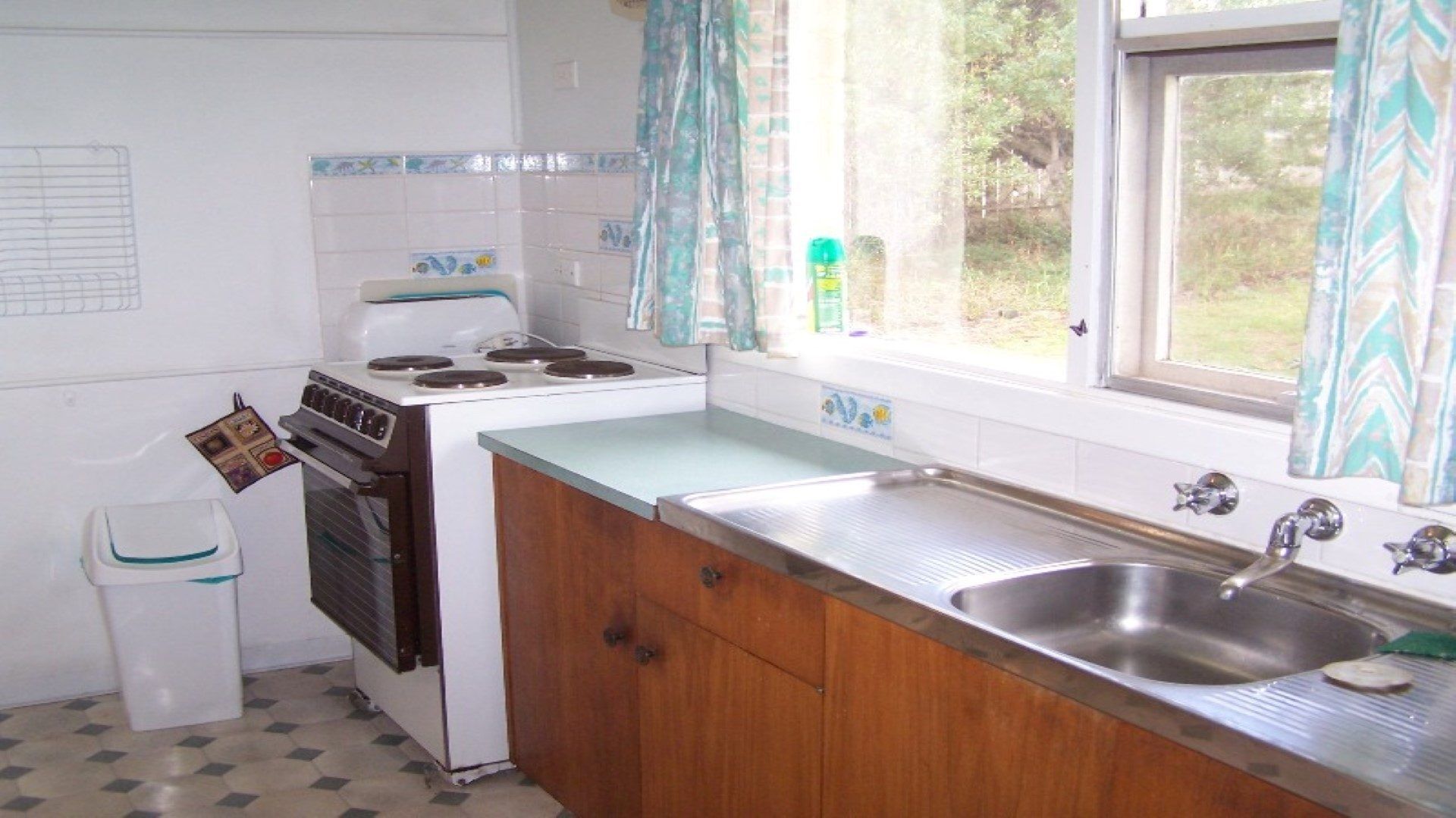 A small kitchen with a stove, sink, and window with curtains.