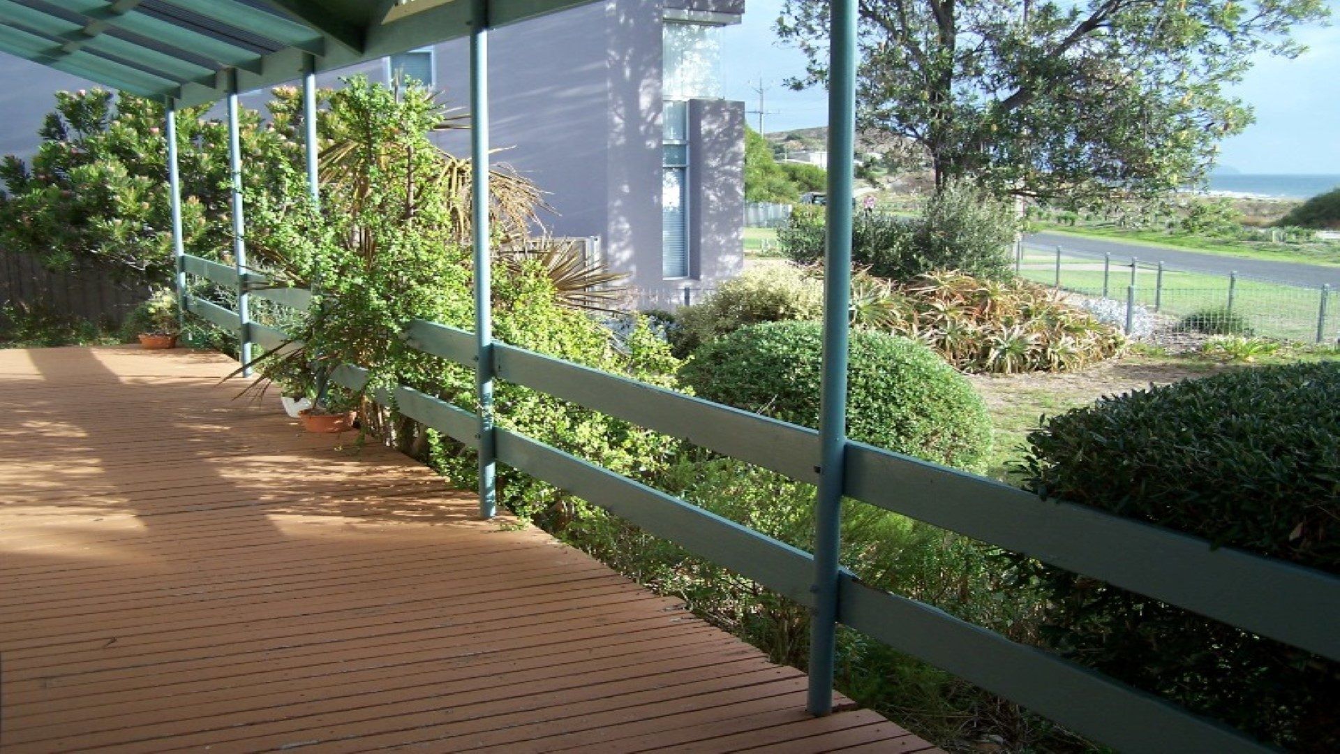 A wooden deck with a metal railing overlooking a landscaped garden and a view of the ocean.