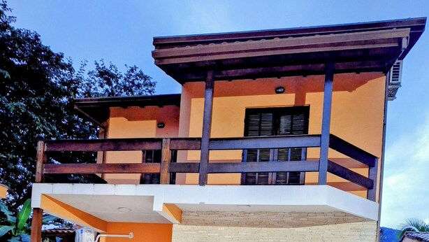 A swimming pool with lounge chairs and a two-story building with a balcony. - Beautiful house with pool and great location (Caraguatatuba)