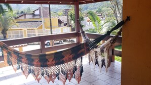 A hammock hanging on a balcony with a view of a residential area and a parked car. - Beautiful house with pool and great location (Caraguatatuba)