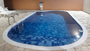 A swimming pool with a tiled floor and metal handrails. - Beautiful house with pool and great location (Caraguatatuba)