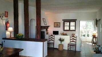 Un salón acogedor con chimenea, sillas de madera, una mesita y un televisor.