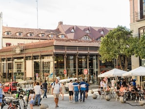 A bustling street scene with pedestrians, outdoor seating, and a building with a distinctive roof.