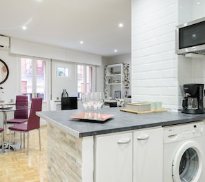 A modern kitchen with a Bosch washing machine, a coffee maker, and a dining area with a glass table and chairs.