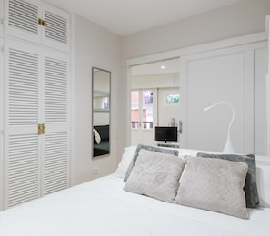 A bedroom with a bed, pillows, a TV, and a mirror.