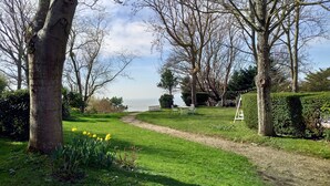 A garden with a path leading to a table and chairs, surrounded by trees and a view of the sea. - The Sea Cottage (Villerville)