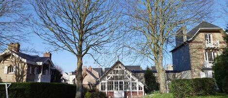 A traditional house with a large tree in front, a well-maintained lawn, and a clear blue sky.