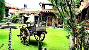 A courtyard with a wooden cart, a fountain, and lush greenery. - COMFORTABLE BEDROOM SALAM FURNISHED OF 25 M2 BUILT IN A HOUSE OF THE XVII CENTURY (Jocotitlan, MEX)
