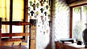 A rustic room with a wooden bench, a wall adorned with crosses, and a window with curtains. - COMFORTABLE BEDROOM SALAM FURNISHED OF 25 M2 BUILT IN A HOUSE OF THE XVII CENTURY (Jocotitlan, MEX)