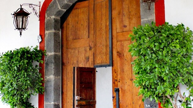 A stone archway leading to a wooden door, flanked by potted plants and a lantern. - COMFORTABLE BEDROOM SALAM FURNISHED OF 25 M2 BUILT IN A HOUSE OF THE XVII CENTURY (Jocotitlan, MEX)