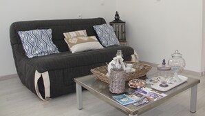 Una sala de estar con un sofá gris oscuro, cojines estampados, una mesa de centro de cristal con revistas, una cesta de mimbre y un farol decorativo.