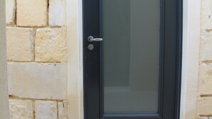 Una puerta oscura con un panel de vidrio, incrustada en una pared de piedra con un escalón que la precede.