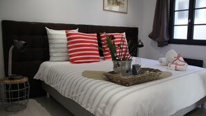 Una cama bien hecha con almohadas a rayas, una lámpara de noche y una mesita con una planta y un vaso.