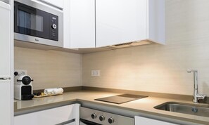 Une cuisine moderne avec des meubles blancs, un four à micro-ondes encastré, une machine à café, un évier et une cuisinière.