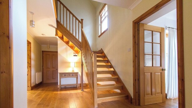 A wooden staircase leading to a second floor, a door with frosted glass panels, and a hallway with wooden flooring.