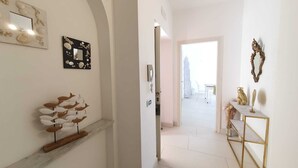 A hallway with a wooden shelf holding decorative items, a mirror with a seashell frame, and a console table with a gold frame and decorative objects. - UVA, Pagliarulo Complex by AMALFIVACATION.IT, Pool, Sea View, 2 Terraces (RAVELLO)