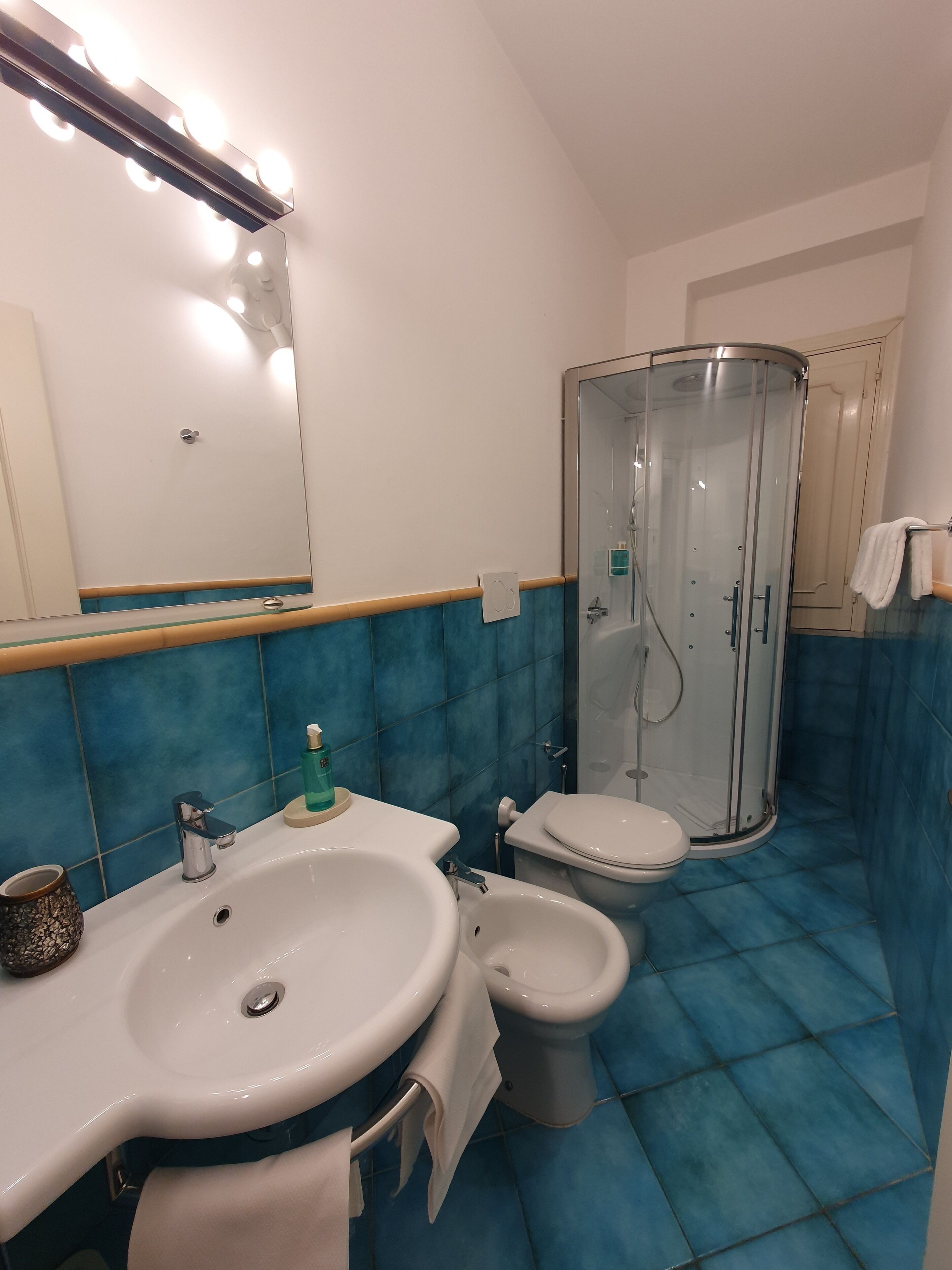 Ein Badezimmer mit einem weißen Waschbecken, einem Bidet, einer Duschkabine und einem beleuchteten Spiegel.