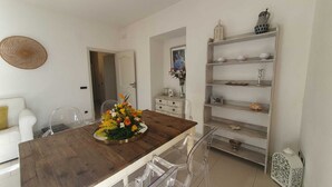 A modern dining area with a wooden table, clear chairs, and a white sofa. A decorative vase with flowers is on the table. - UVA, Pagliarulo Complex by AMALFIVACATION.IT, Pool, Sea View, 2 Terraces (RAVELLO)