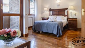Ein Schlafzimmer mit einem Holz-Kopfteil, zwei Nachttischen mit Lampen, einem großen Fenster und Blick auf die Straße.