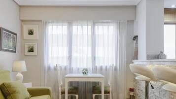 Een gezellige woonkamer met een groene bank, een witte tafel met stoelen, en een keuken met een achterwand van steen.