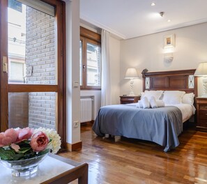 A bedroom with a wooden headboard, two bedside tables with lamps, a large window, and a view of the street. - Argüelles, cozy apartment for 4 in the center, AC (Madrid)