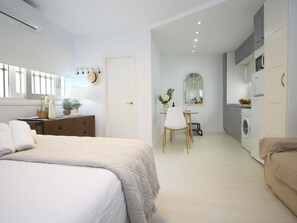 Ett sovrum med en säng, en byrå, ett skrivbord med en stol, ett matbord med stolar, ett köksområde med vitvaror och ett badrum med toalett och handfat.