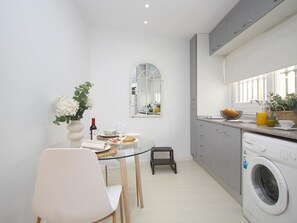 Une cuisine compacte avec une table à manger en verre, un lave-linge et un petit tabouret.