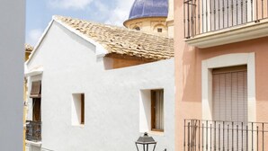 A narrow street with buildings featuring traditional architecture, including a dome and a balcony with a railing.