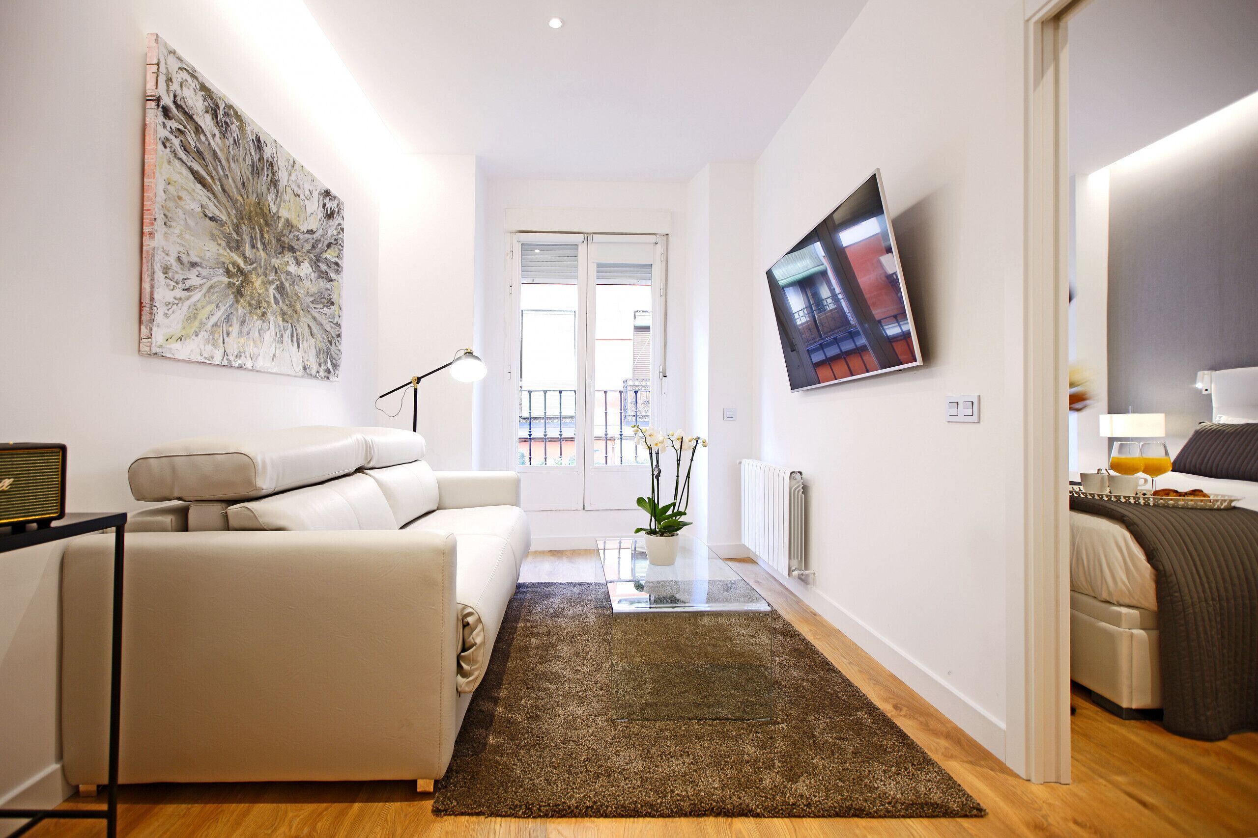 A modern living room with a sofa, a coffee table, a rug, and a TV on the wall.
