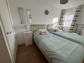 A bedroom with two beds, a nightstand, a dresser, a mirror, and a window with curtains. - Seaways, in Sandown,for a great relaxing holiday, Family friendly, free parking (Isle of Wight)