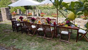 Un área de comedor al aire libre con paredes de piedra, sillas y mesas de madera decoradas con flores, frutas y bebidas.