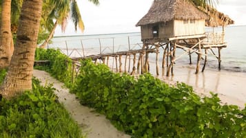 Ein Strandbungalow mit Reetdach, einer Holzterrasse und Blick aufs Meer.
