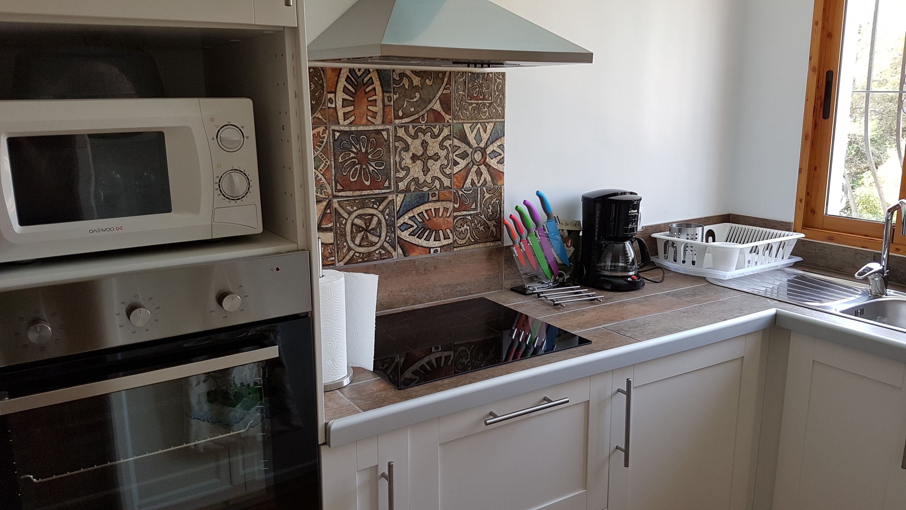 A kitchen with a microwave, oven, coffee maker, and a tiled backsplash.