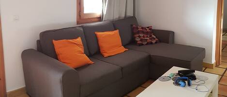 Un saló amb un sofà, dos coixins taronja, una taula de cafè blanca i una finestra amb cortines.
