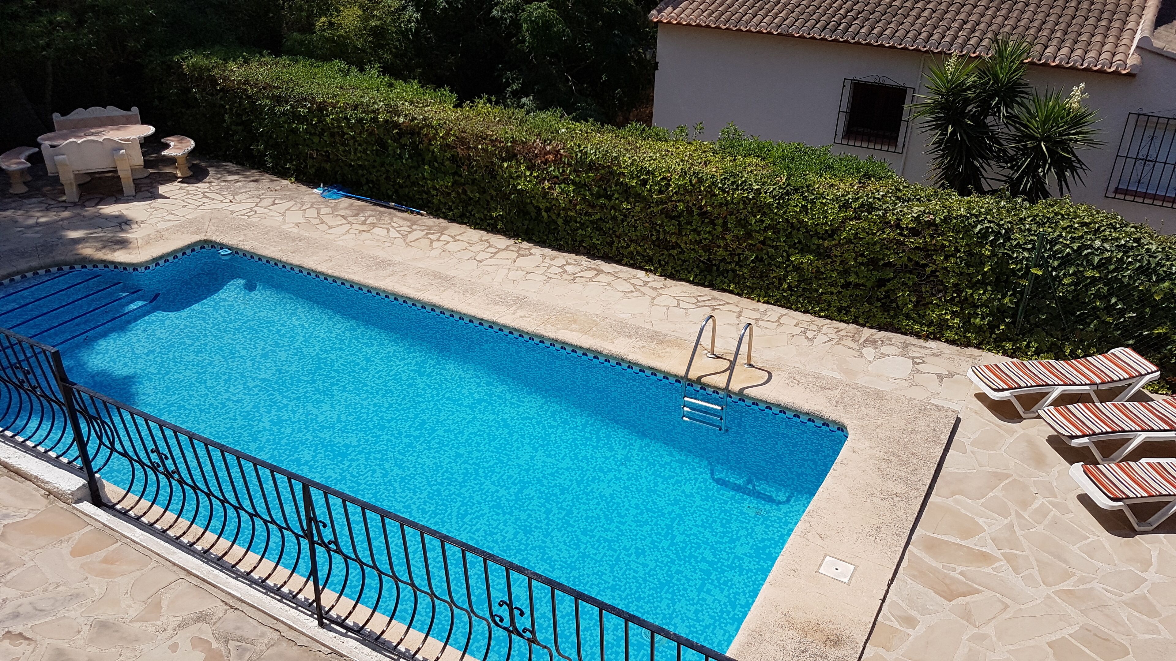 Ein rechteckiger Pool mit einer Steindeckung, umgeben von einem Metallzaun.