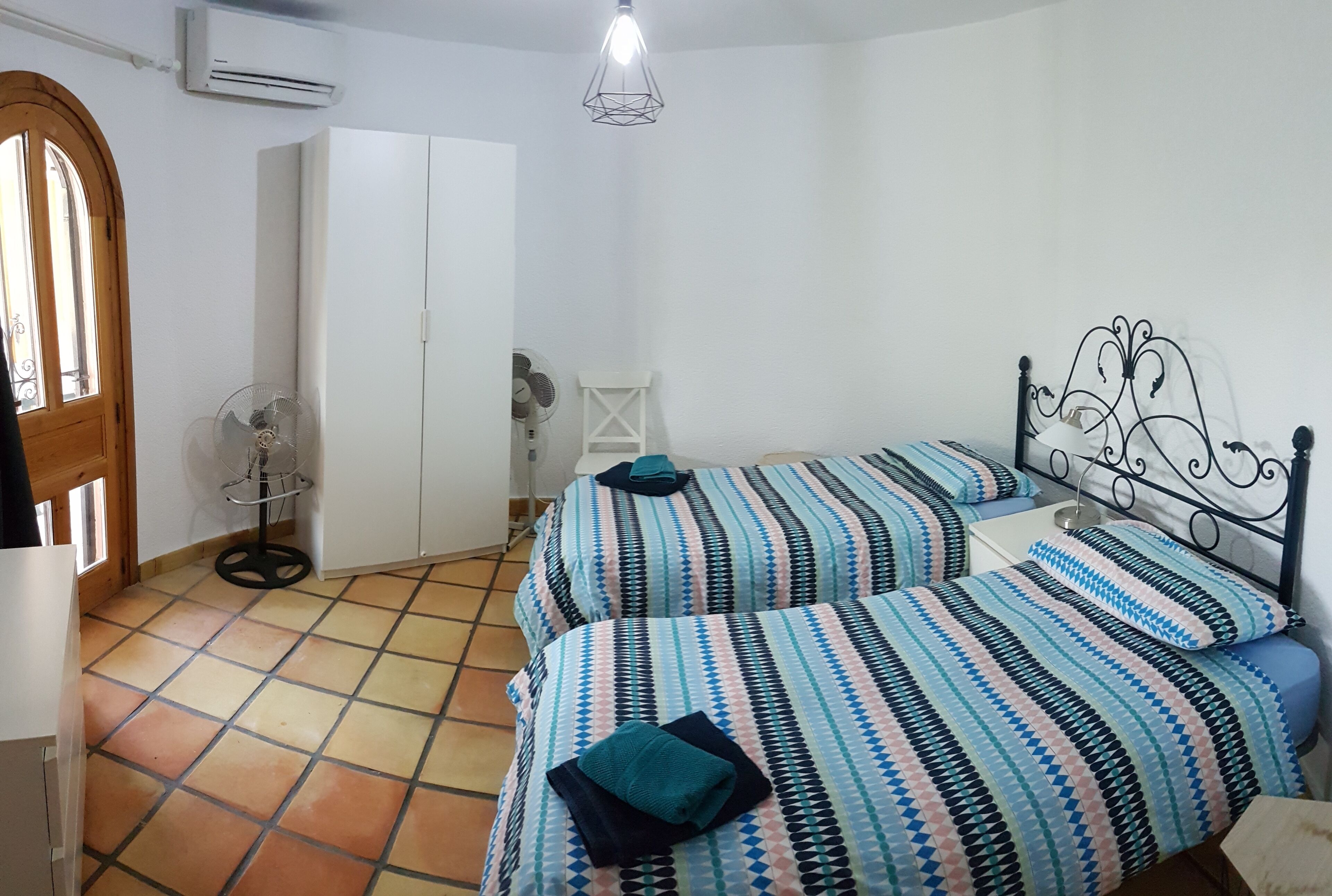 Une chambre avec deux lits, un ventilateur et une armoire.