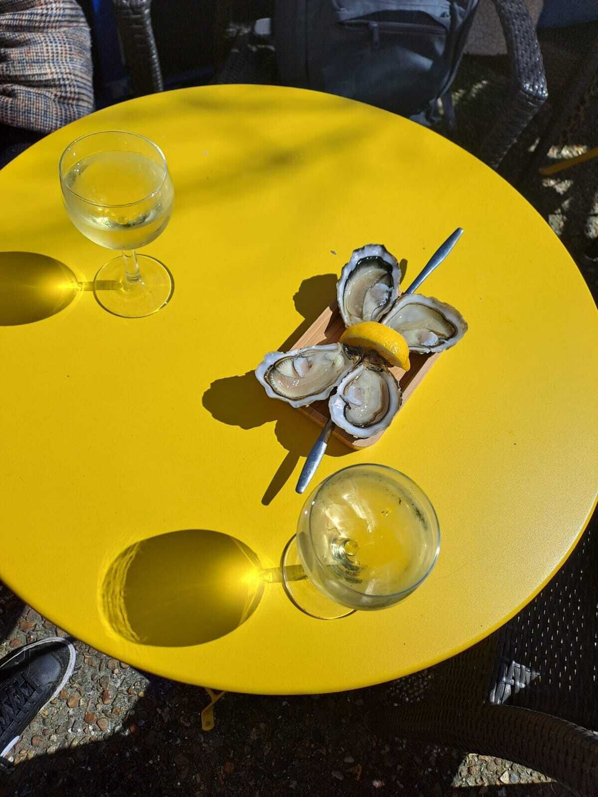 Una mesa amarilla con tres copas de vino y un plato de ostras.