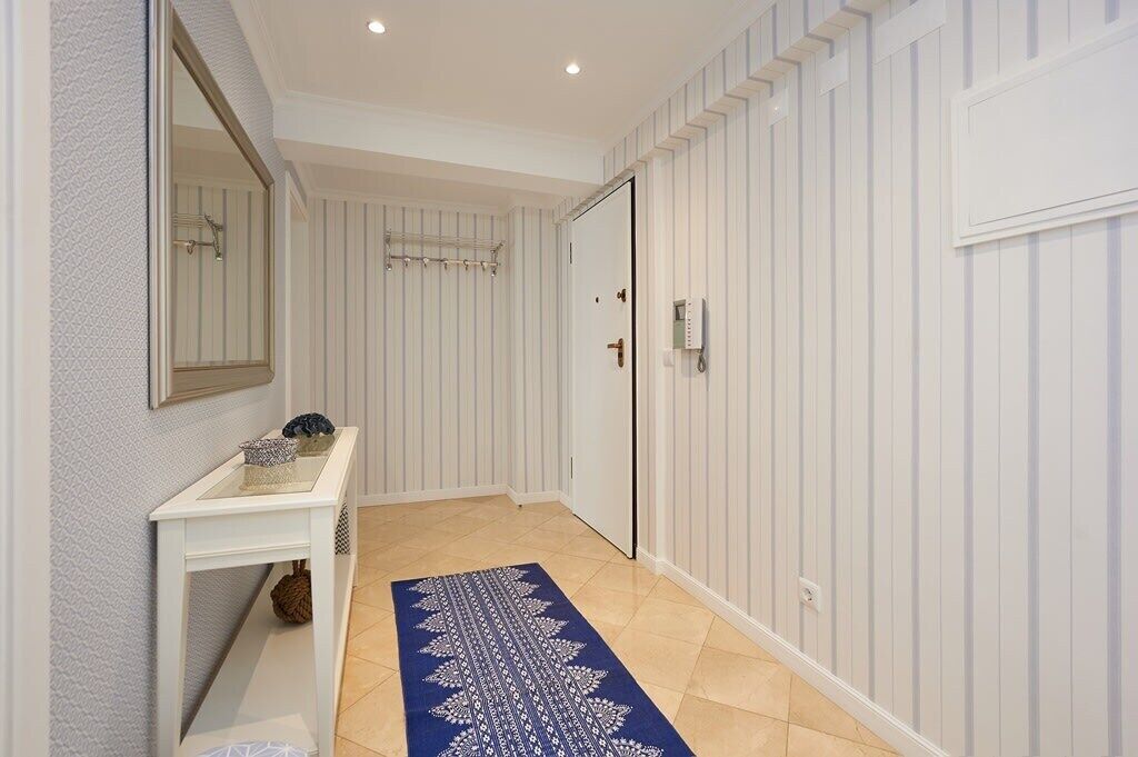 Un couloir avec une porte blanche, une petite table ornée d’objets décoratifs et un tapis à motifs.