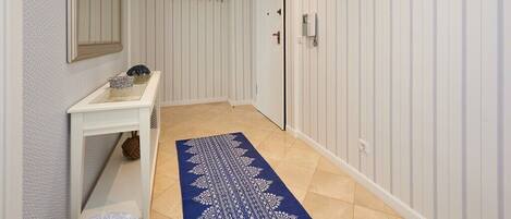 Un couloir avec une porte blanche, une petite table ornée d’objets décoratifs et un tapis à motifs.