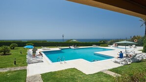 A swimming pool with a view of the ocean, surrounded by lounge chairs and umbrellas. - Oceanario Apartment by Portugal Portfolio (Cascais)